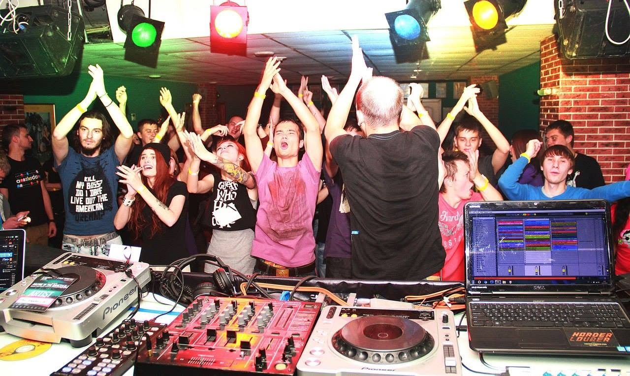 A crowd with raised hands seen from behind the DJ booth